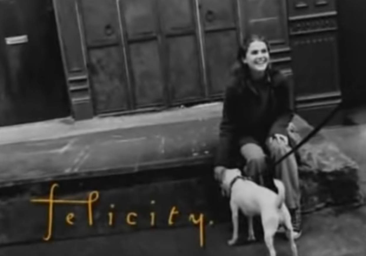 A still from the opening credits of Felicity, with Felicity sitting on a concrete smiling, while petting a dog. The image is in black and white. Felicity is looking at someone who is out of the frame